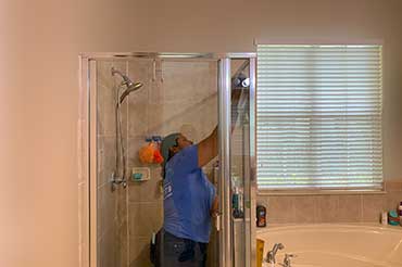 A woman cleaning a shower glass, removing soap scum for a spotless bathroom